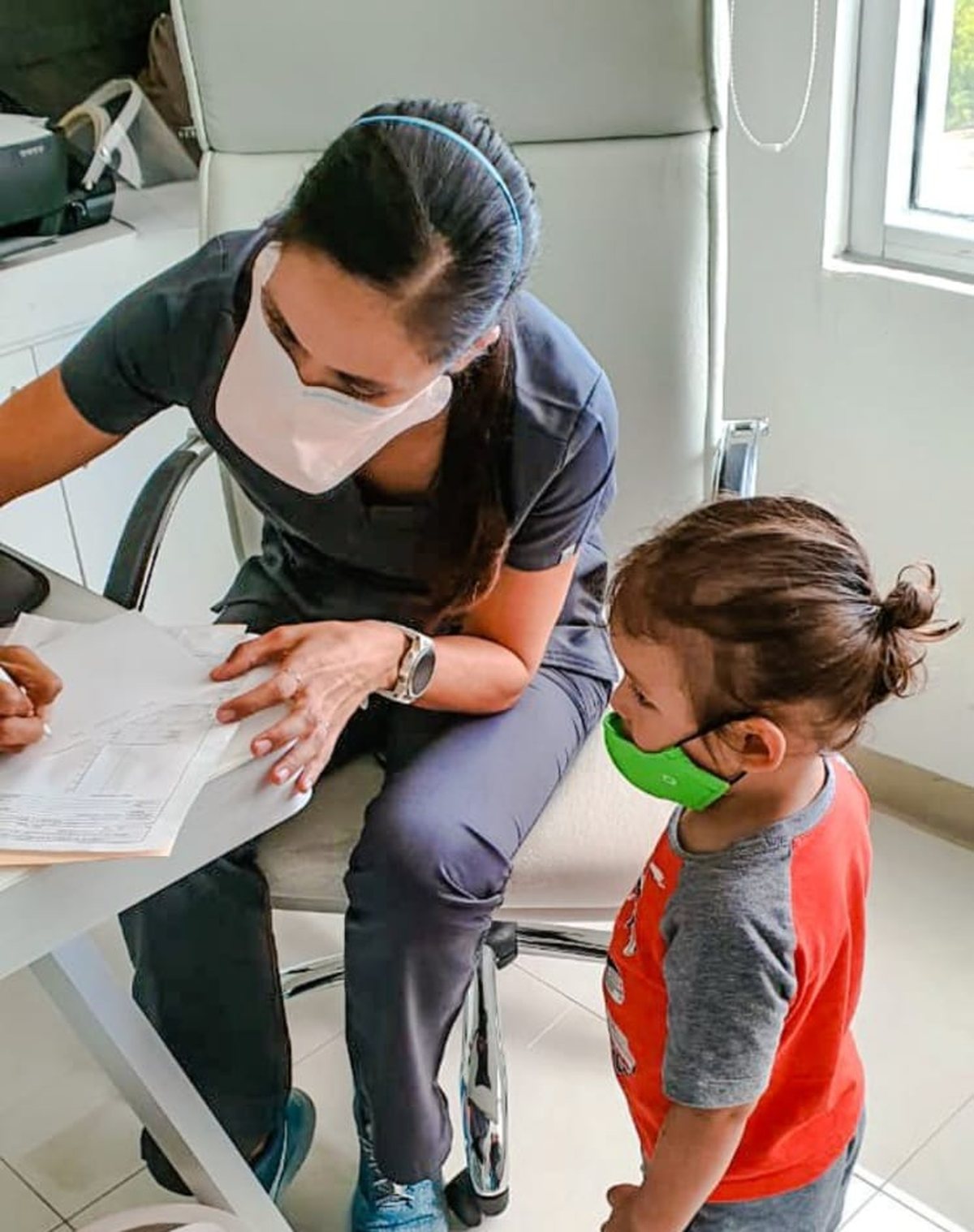 Un niño pequeño observa en consulta mientras se llena su expediente clínico