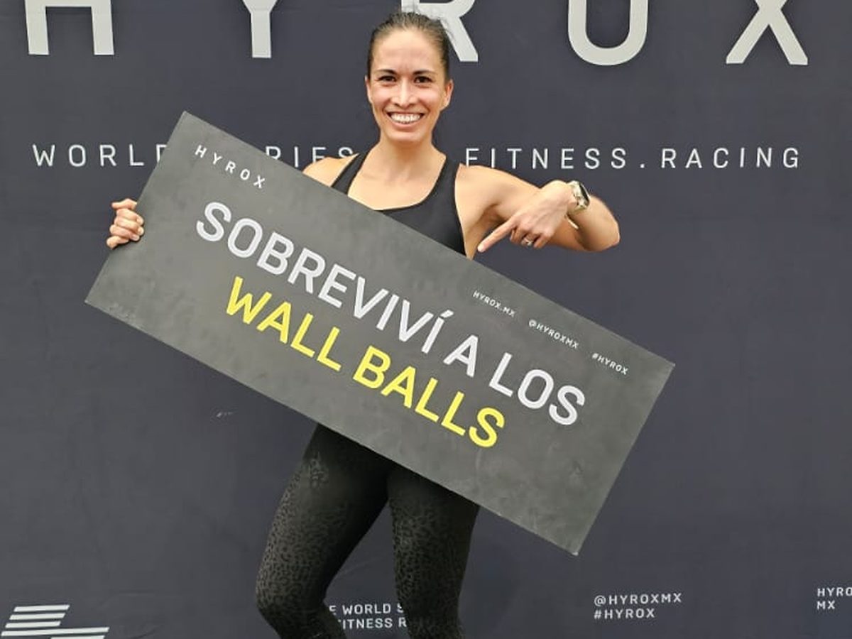 La Dra. Lili Padilla sonriendo en una competencia HYROX, sosteniendo un letrero